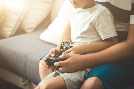 Father and son holding a joystick controllers while playing a video games at home.