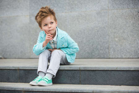 Fashion baby boy in mint jacket and sneakers posing on a gray wall background. Trendy boy standing on the street.の写真素材