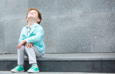 Fashion baby boy in mint jacket and sneakers posing on a gray wall background. Trendy boy standing on the street.の写真素材