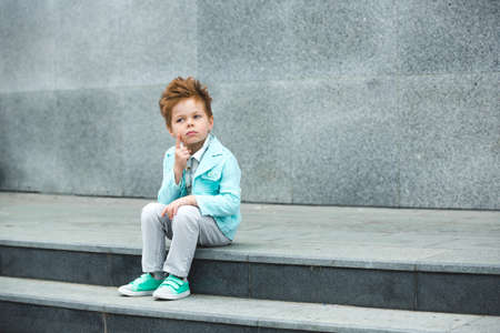 Fashion baby boy in mint jacket and sneakers posing on a gray wall background. Trendy boy standing on the street.の写真素材