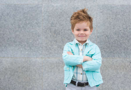 Fashion baby boy in mint jacket posing on a gray wall background. Trendy boy standing on the street.の写真素材