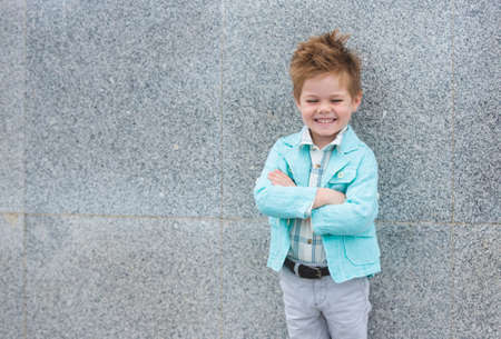 Fashion baby boy in mint jacket posing on a gray wall background. Trendy boy standing on the street.の写真素材