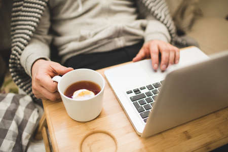 Young man laying in bad with laptop and cup of tea in hand.の写真素材