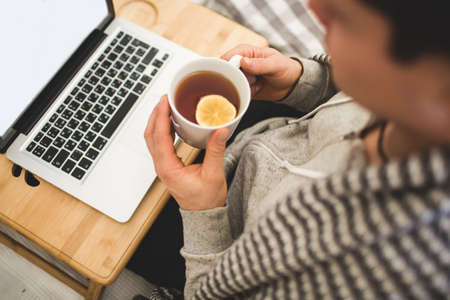 Young man laying in bad with laptop and cup of tea.
