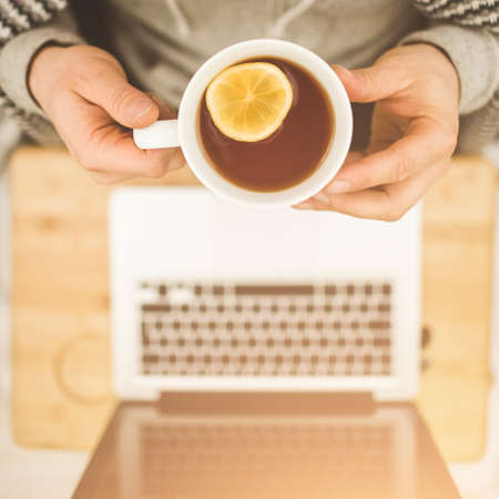 Top view hands with cup of tea with lemon and laptop on the table.の写真素材
