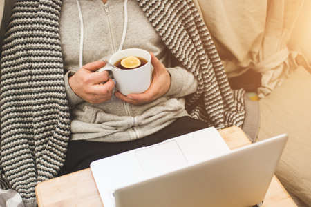 Young man laying in bad with laptop and cup of tea in hand.