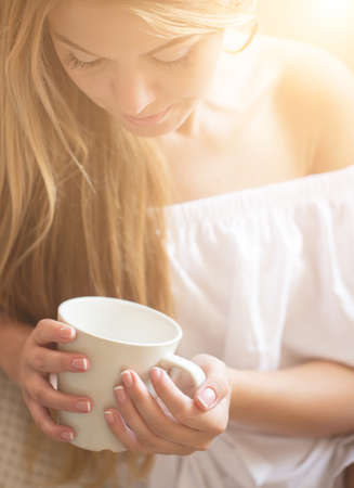 Beautiful young woman relaxing at living room while enjoying in coffee.の写真素材