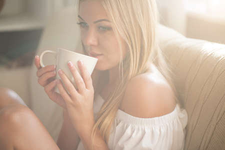 Beautiful young woman relaxing at living room while enjoying in coffee.の写真素材