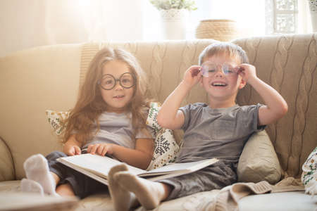 Brother and sister reading a book on the sofaの写真素材