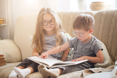 Brother and sister reading a book on the sofaの写真素材