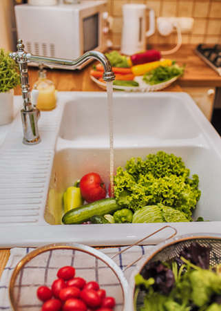 Fresh vegetables under water stream in colanderの写真素材