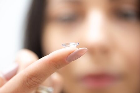 Close portrait of a beautiful woman putting on contact lenses. The contact lens lies on the tip of the finger. Vision correction conceptの写真素材