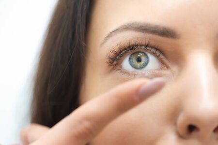 Close portrait of a beautiful woman putting on contact lenses. The contact lens lies on the tip of the finger. Vision correction conceptの写真素材