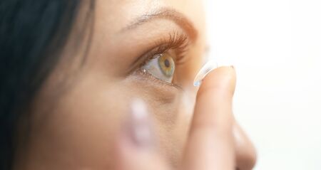 Close portrait of a beautiful woman putting on contact lenses. The contact lens lies on the tip of the finger. Vision correction conceptの写真素材