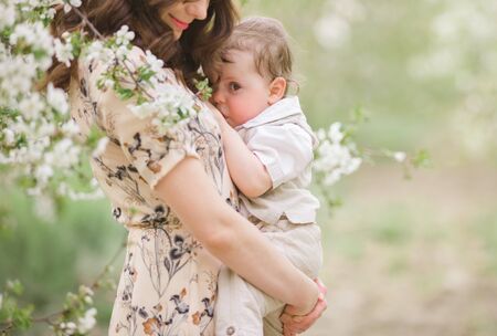 Beautiful young brunette in a colorful dress with her baby. Mother is breastfeeding her baby....