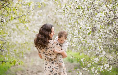 Beautiful young mom plays with her son in the spring garden. Holidays in the villageの写真素材