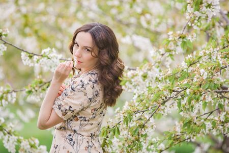 Elegant slender woman enjoys relaxing in the blooming cherry orchard. Holidays in the villageの写真素材