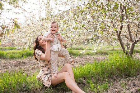 Beautiful young mom plays with her son in the spring garden. Holidays in the villageの写真素材