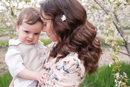 Beautiful young mom plays with her son in the spring garden. Holidays in the villageの写真素材