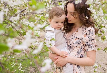 Beautiful young mom plays with her son in the spring garden. Holidays in the villageの写真素材