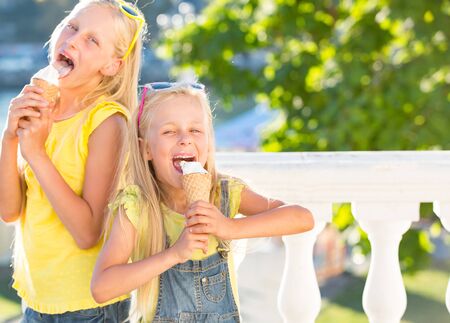 Two sisters  enjoy ice cream in a vaiel glass. Teenagers are fashionably dressed. Children posing against the backdrop of street sceneryの写真素材