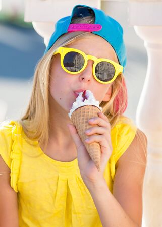 Little girl enjoy ice cream in a vaiel glass. Teen is fashionably dressed. Child posing against the backdrop of street sceneryの写真素材