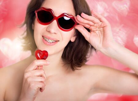 Beautiful girl with perfect skin and multi-colored braces posing with small heart in handの写真素材