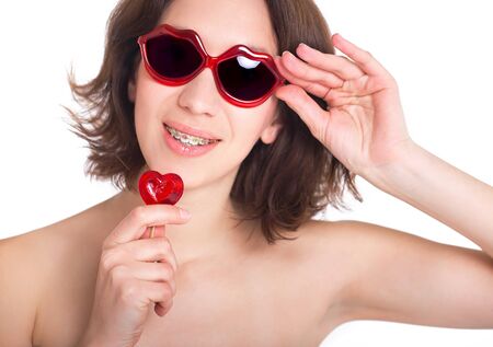 Beautiful girl with perfect skin and multi-colored braces posing with small heart in handsの写真素材