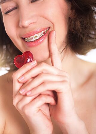 Beautiful girl with perfect skin and multi-colored braces posing with small heart in handsの写真素材