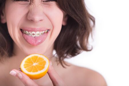 Beautiful girl with perfect skin and multi-colored braces posing with lemon on palmの写真素材