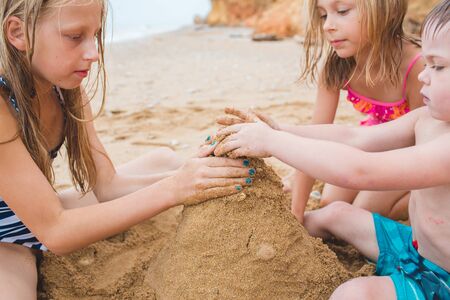 Brother and sisters are playing with sand on the beach. Build castles from sand. Lifestyle photoの写真素材