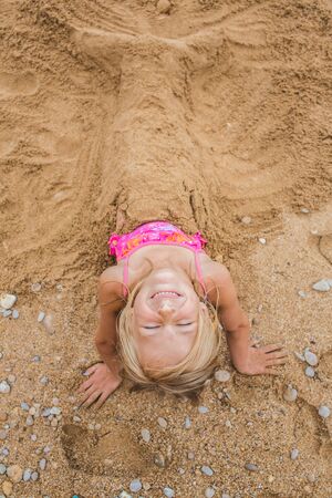 Little girl playing with sand on the beach. Build castles from sand. Lifestyle photo view from aboveの写真素材