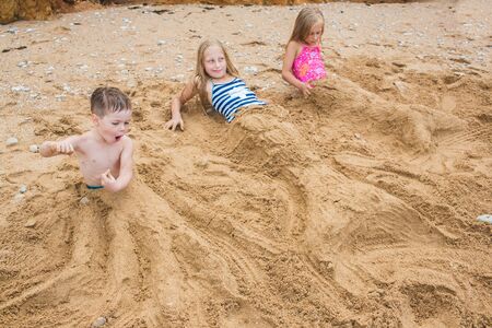 Brother and sisters are playing with sand on the beach. Lifestyle photoの写真素材