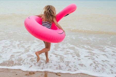 A girl is playing on the beach with an inflatable flamingo. the hit of the seasonの写真素材