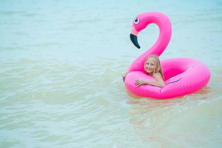 A girl is playing on the beach with an inflatable flamingo. the hit of the seasonの写真素材