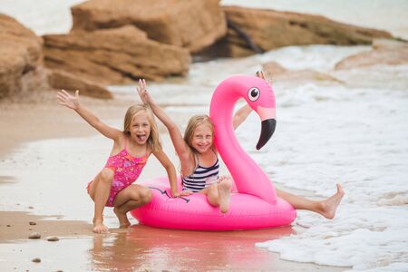 Girls are playing on the beach with an inflatable flamingo. the hit of the season. two sistersの写真素材
