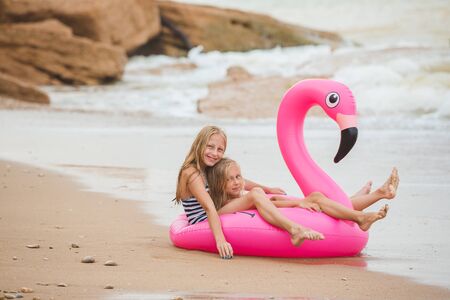 Girls are playing on the beach with an inflatable flamingo. the hit of the season. two sistersの写真素材