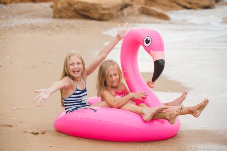 Girls are playing on the beach with an inflatable flamingo. the hit of the season. two sistersの写真素材