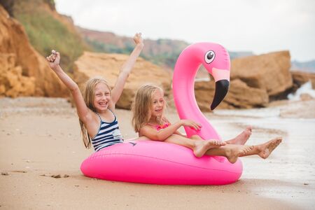 Girls are playing on the beach with an inflatable flamingo. the hit of the season. two sistersの写真素材