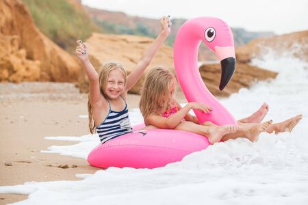 Girls are playing on the beach with an inflatable flamingo. the hit of the season. two sistersの写真素材