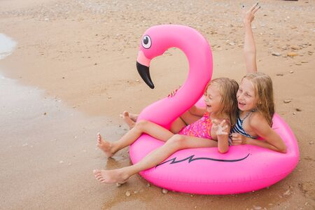 Girls are playing on the beach with an inflatable flamingo. the hit of the season. two sistersの写真素材