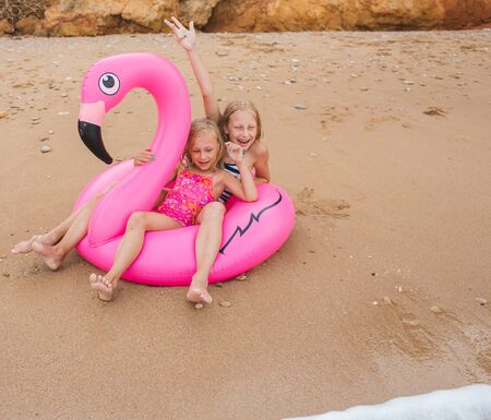 Girls are playing on the beach with an inflatable flamingo. the hit of the season. two sistersの写真素材