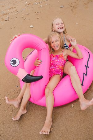 Girls are playing on the beach with an inflatable flamingo. the hit of the season. two sistersの写真素材