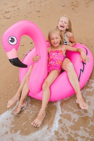 Girls are playing on the beach with an inflatable flamingo. the hit of the season. two sistersの写真素材
