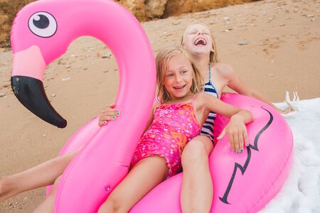 Girls are playing on the beach with an inflatable flamingo. the hit of the season. two sistersの写真素材