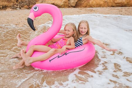 Girls are playing on the beach with an inflatable flamingo. the hit of the season. two sistersの写真素材