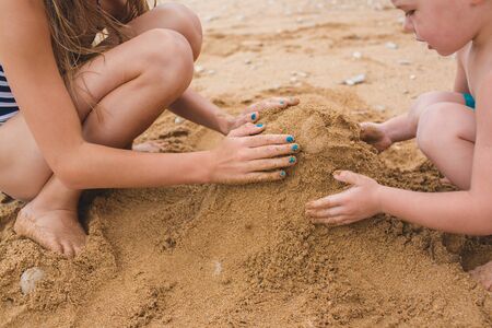 Brother and sister are playing with sand on the beach. Build castles from sand. Lifestyle photoの写真素材