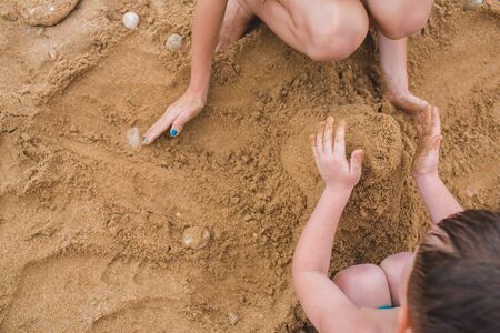 Brother and sister are playing with sand on the beach. Build castles from sand. Lifestyle photoの写真素材