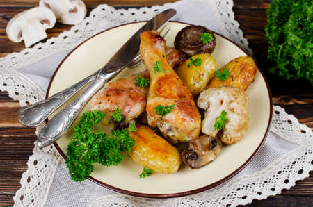 Baked chicken drumsticks with potatoes, mushrooms and cauliflower served on a wooden table. Rustic styleの写真素材