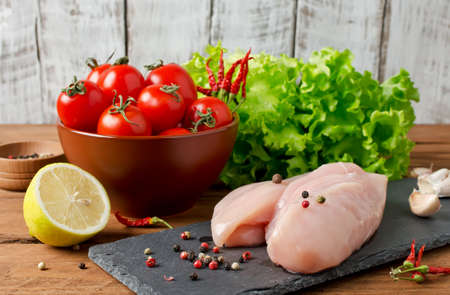 Fillets, olive oil, tomatoes, spices and salad leaves on wooden backgroundの写真素材